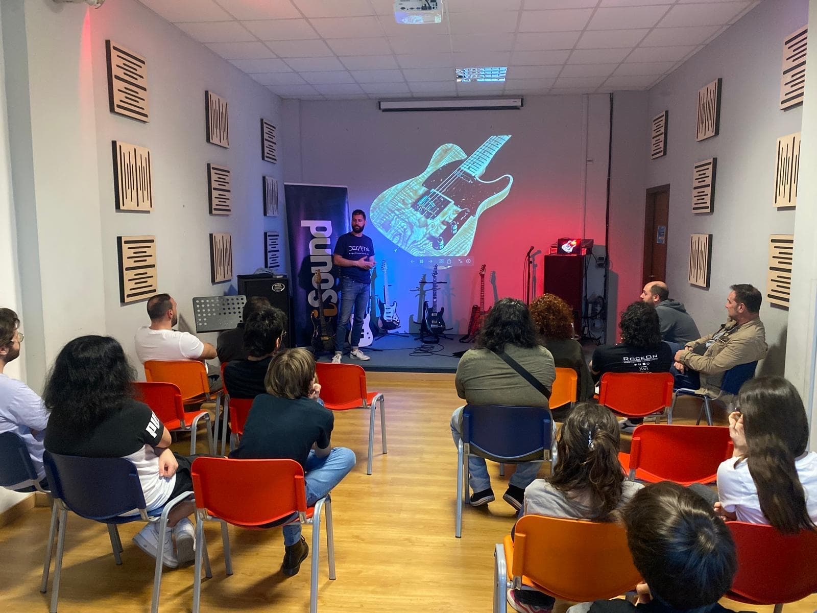 La sala vista dal fondo, con il pubblico seduto e il palco illuminato