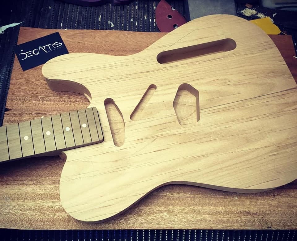 The body of a De Gattis Thinline just milled from bare wood, on the workshop bench, with the fretboard resting beside it